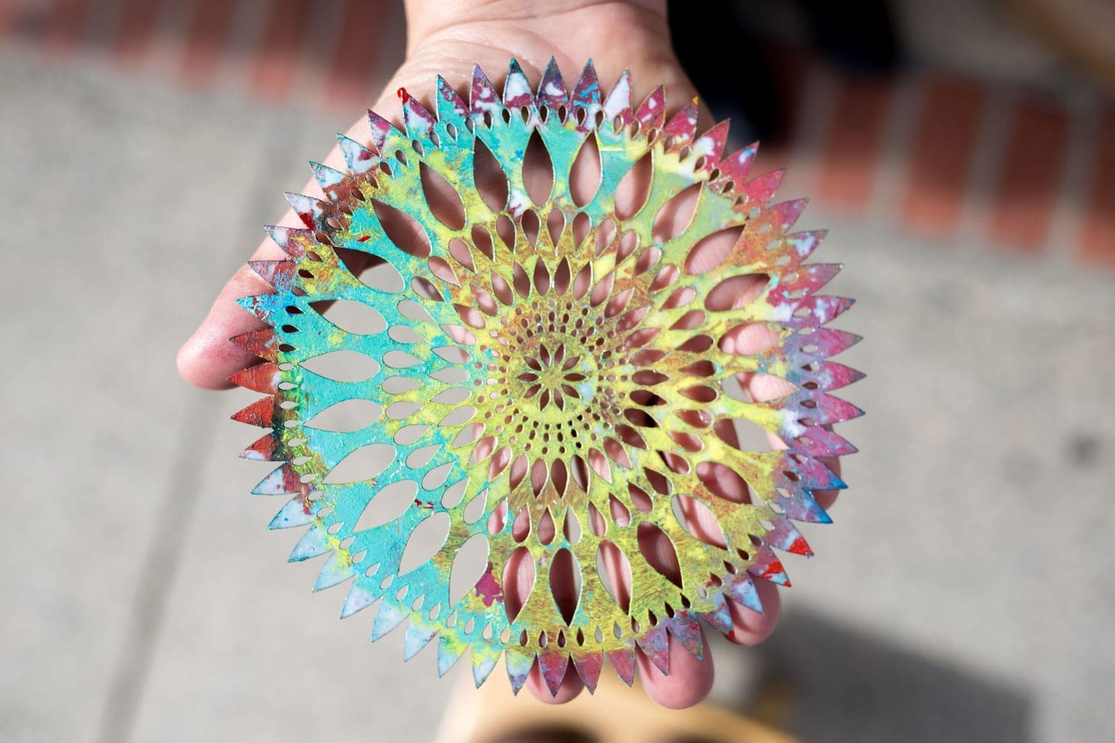 A hand holding a colorful, hand-painted filigree art piece made in the studio.