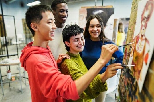 Smiling young adults painting on canvases together in a bright art studio.
