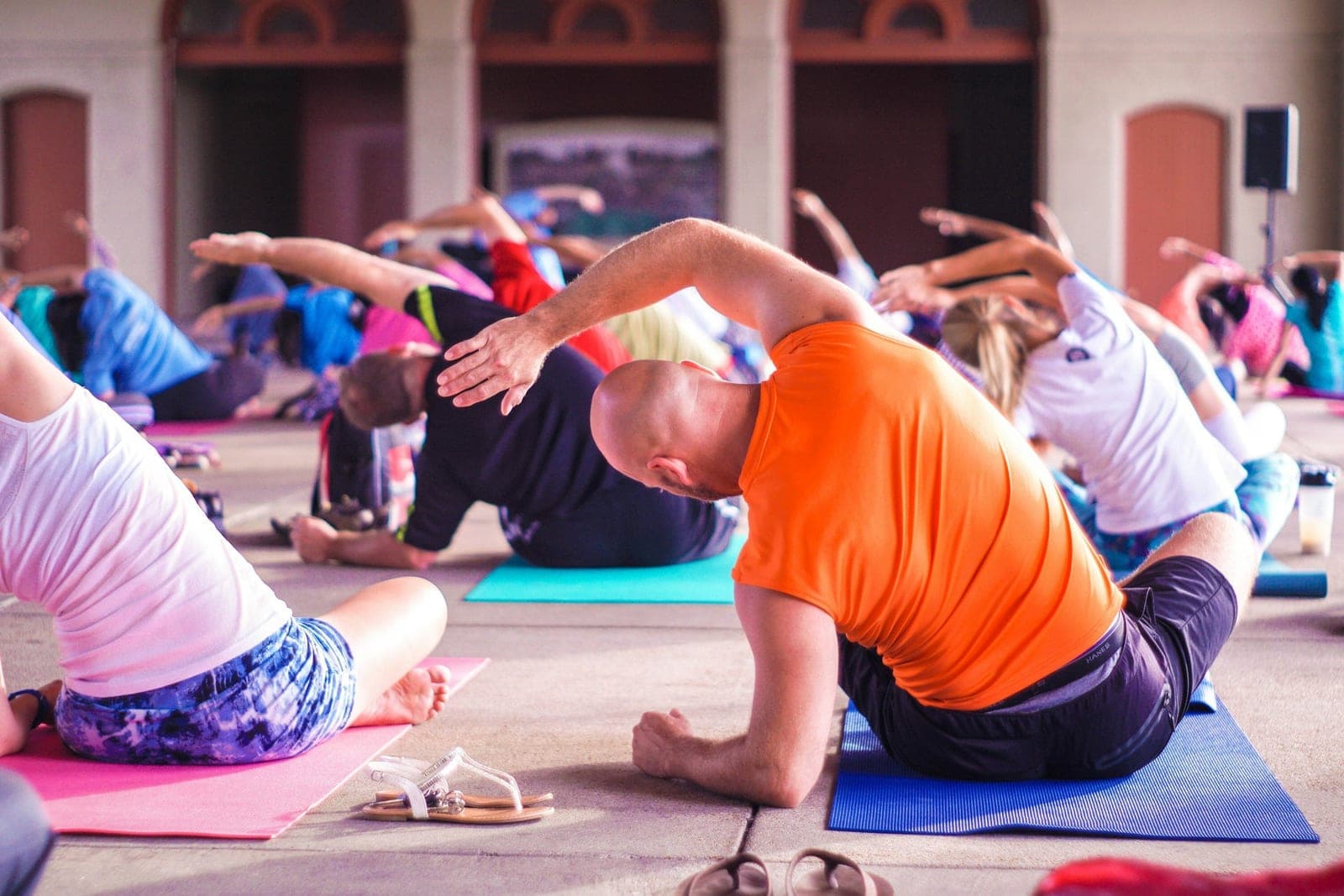 A group of adults on yoga mats moving through a seated side-stretch pose together in a bright, open space.