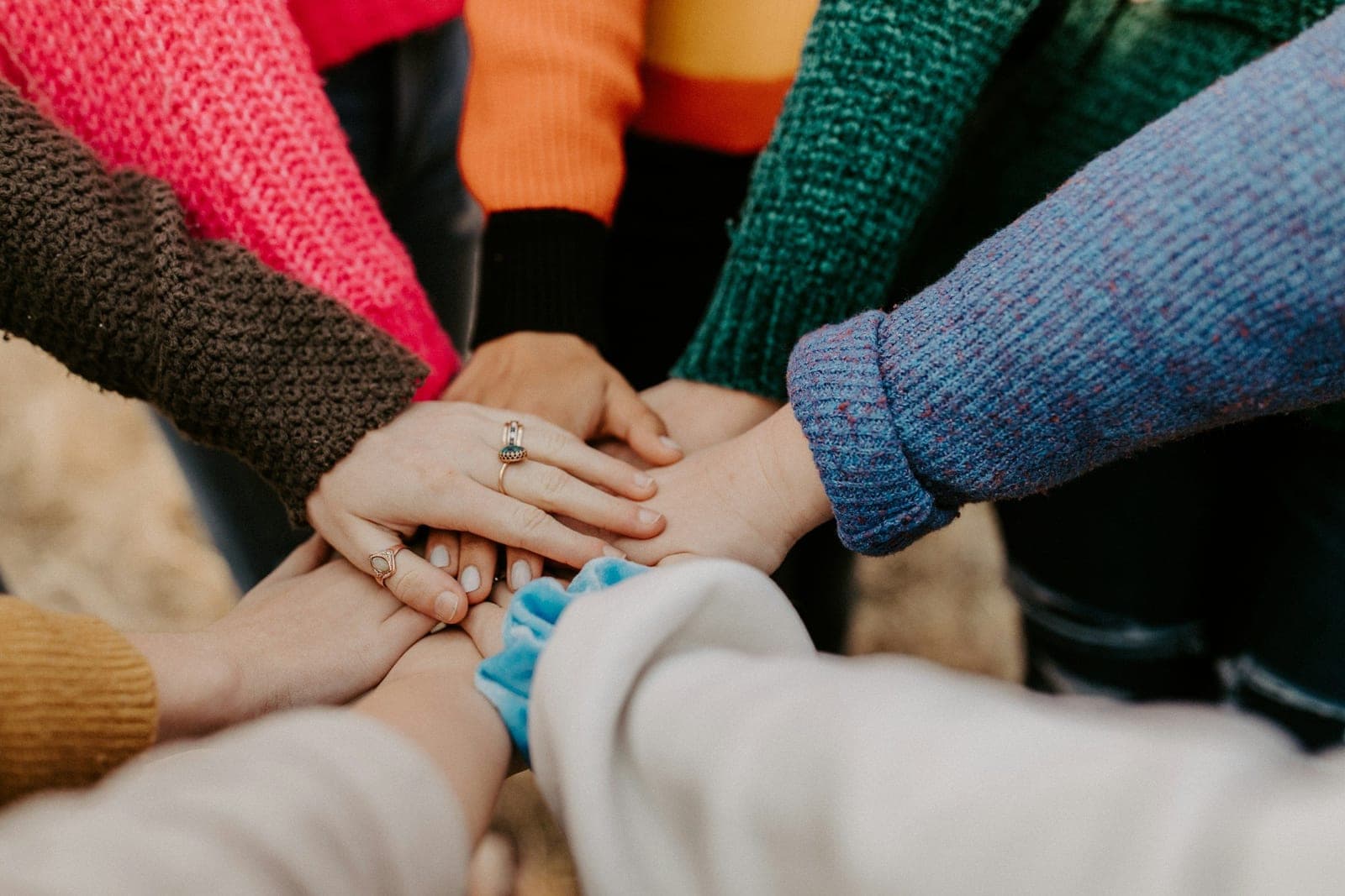 A group of teens in colorful sweaters stacking their hands together in the center as a sign of connection and teamwork.